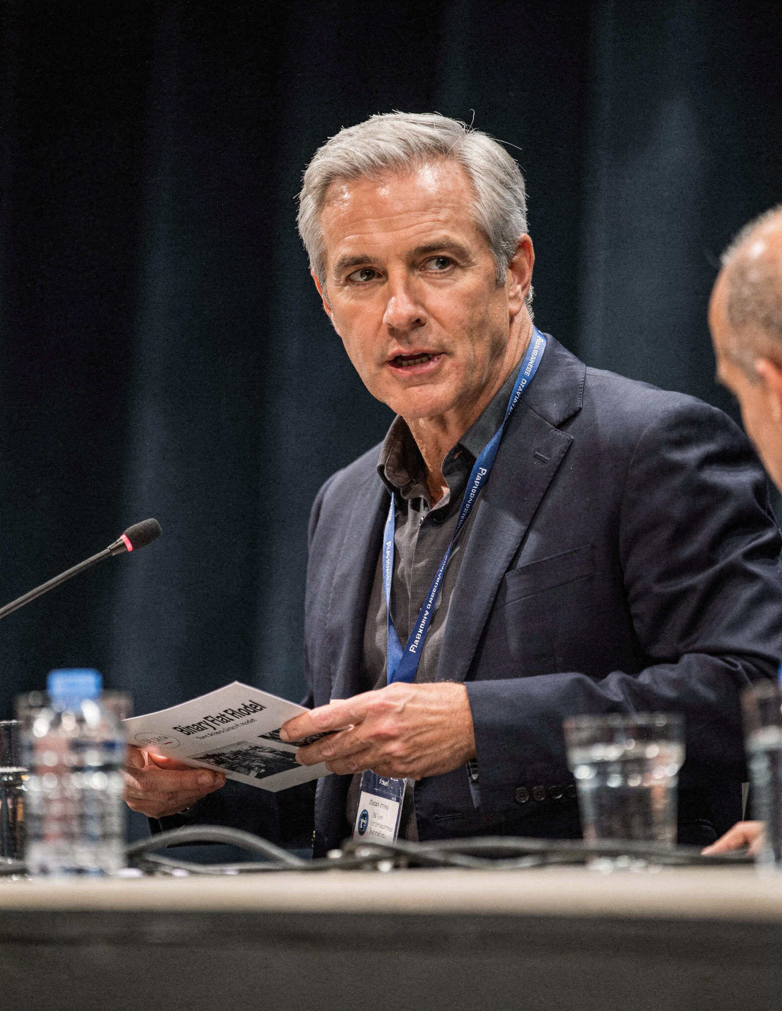 Julian Mercer seated at a Janus Earth panel table with microphone and papers